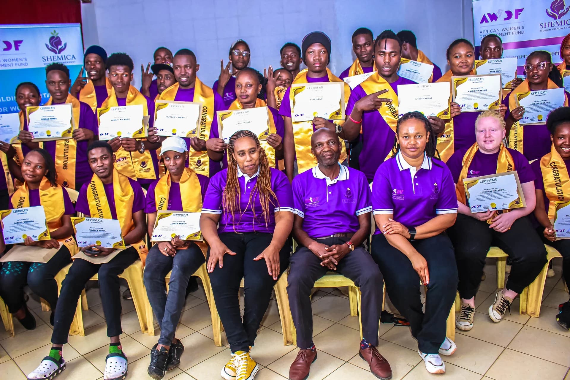 A closer view of graduates in purple shirts displaying their certificates.