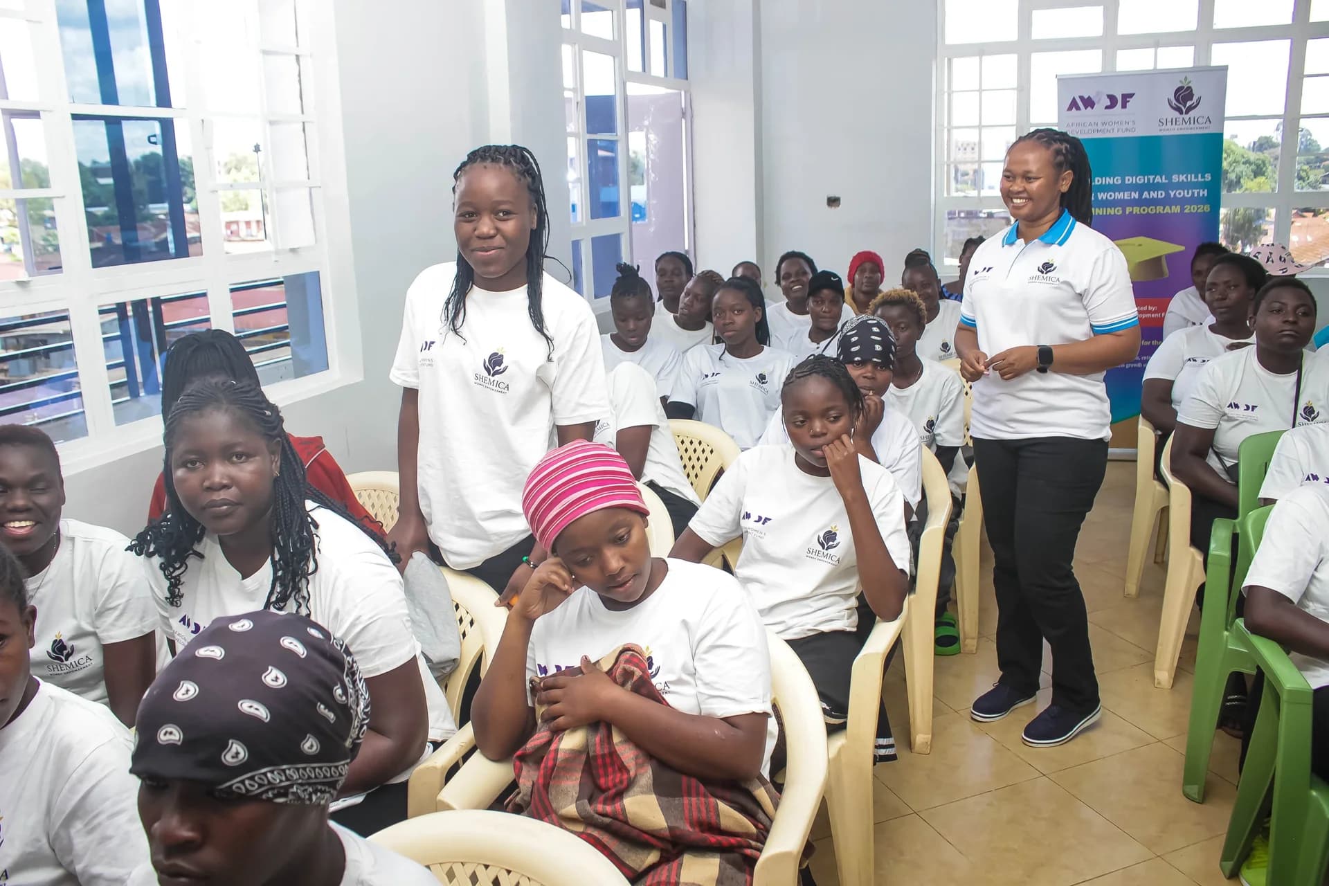 A learner stands to speak while a facilitator and classmates listen.